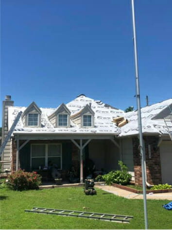 House roof being repaired with shingles partially removed under clear blue sky