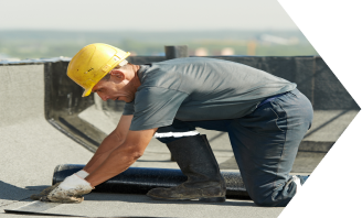 Construction worker in yellow hard hat installing roofing materials on flat roof